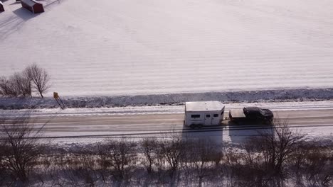 Truck-towing-white-horse-trailer-on-rural-road-in-winter-season,-aerial-drone-shot