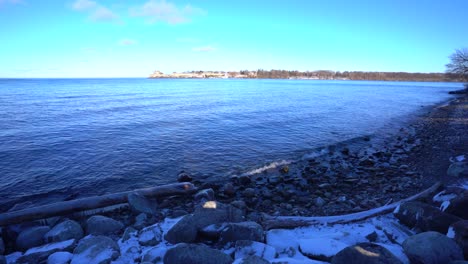 Niagara-on-the-lake-rocky-shore-beach-during-winter-with-snow-and-ice-as-waves-come-crashing-to-shoreline---Ontario,-Canada