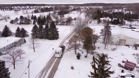 Hauling-white-horse-trailer-through-small-winter-town-in-Michigan,-aerial-drone-shot