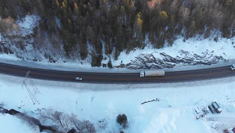 Vehicles-Passing-Through-Highway-In-Snowy-Winter-Landscape---aerial-shot