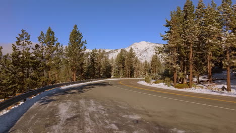 Cars-drive-past-on-a-mountain-road-as-camera-booms-up-to-reveal-mountains-and-blue-sky-on-horizon-in-Lake-Tahoe,-Nevada