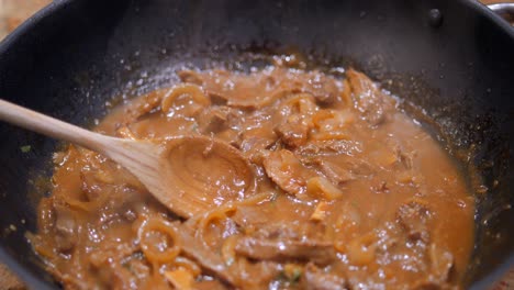 Close-up-of-huge-wok-while-cooking-sauteed-beef-stew-with-onions,-soy-sauce-and-coriander-in-a-light-brown-sauce