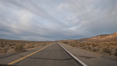 Driving-along-a-southern-California-highway-passing-a-wind-turbine-farm-in-the-Mojave-Desert-foothills---hyper-lapse