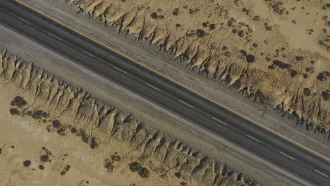 Aerial-Looking-Down-As-Car-Passes-Along-Empty-Diagonal-Road-Through-Desert-Landscape-In-Balochistan