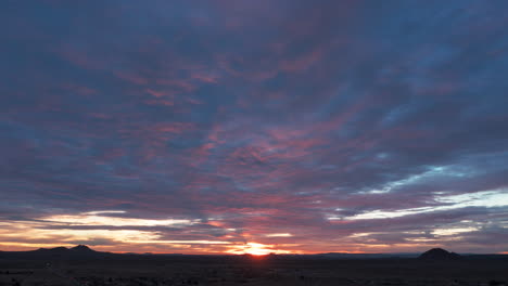 A-wave-of-crimson-clouds-precedes-the-golden-dawn-of-a-new-day-in-the-Mojave-Desert---aerial-hyper-lapse