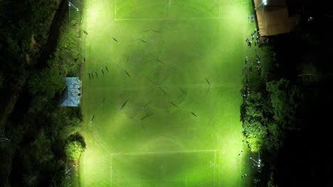 Aerial-top-down-of-two-sport-teams-playing-soccer-at-night-in-an-illuminated-grass-field
