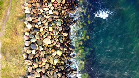 Drone-footage-From-a-Birds-Perspective-Flying-Over-Rocks-at-a-Coast-with-Water-Splashing-Towards-Them