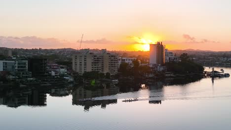 Three-coxed-foursome-row-boats-are-racing-up-a-still-Brisbane-river-as-the-sunrises-in-the-distance