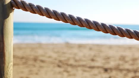 Isolated-view-of-a-rope-with-the-beach-and-ocean-in-the-background---rope-acts-as-a-safety-railing-for-a-boardwalk