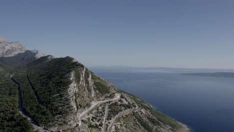 drone-video-over-the-mountain-pass-of-the-homeland-war-on-the-Makarska-riverbank,-frontal-shot-moving-forward-leaving-the-road-behind-and-ending-on-the-top-of-the-mountain