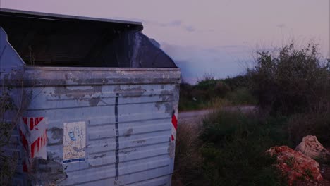 A-trash-dumpster-and-litter-at-the-side-of-the-road-with-cars-speeding-by-at-sunset---static-time-lapse