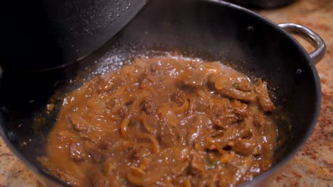 Lid-covering-and-uncovering-wok-while-cooking-sauteed-beef-stew-with-onions,-soy-sauce-and-coriander-in-a-light-brown-sauce
