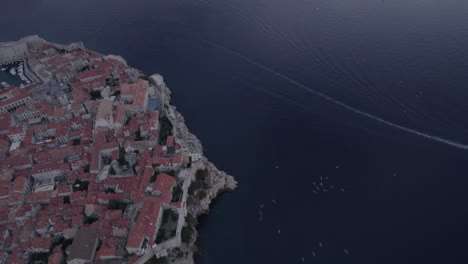 drone-video-in-Dubrovnik-with-the-island-of-Lokrum-on-the-main-and-the-city-on-the-side-with-yacht,-canoes-and-speedboats,-sunset