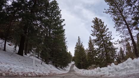 Icy-winter-road-in-the-Tehachapi,-California-mountains-with-snow-accumulation-and-a-cloudscape-overhead---time-lapse
