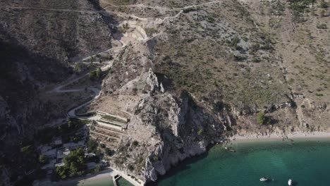 drone-video-over-Zadvarje-Beach-on-the-coast-of-Crocia-located-on-the-Makarska-Riviera,-boats-are-seen