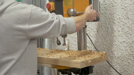 Young-man-using-pillar-drill-drilling-holes-in-white-oak-slab