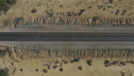 Aerial-Looking-Down-As-Car-Passes-Along-Empty-Road-Through-Desert-Landscape-In-Balochistan