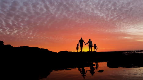 Family-on-rocky-coastline-enjoy-fire-sunset