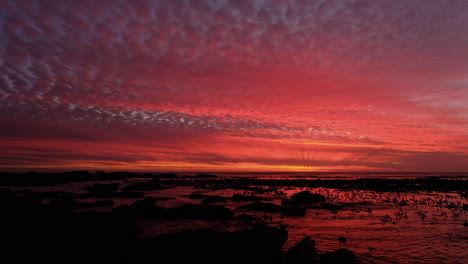 Tilt-up-shot-of-vivid-sunset-illuminating-clouds-on-rocky-coastline