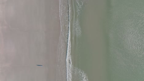 Waves-along-coastline-looking-down-at-person-walking-on-beach