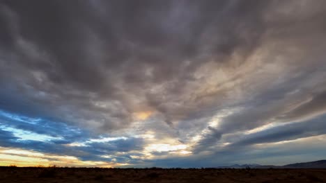 Dramatic-overcast-sunset-sky-above-the-Mojave-Desert's-harsh-and-rugged-landscape---wide-angle-time-lapse