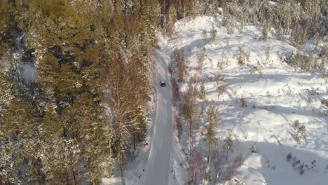 Aerial-View-Of-A-Snowy-Pine-Forest-And-Road-With-Car-Driving-During-Daytime---drone-shot