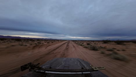 An-off-road-vehicle-speeding-through-the-rugged-terrain-of-the-Mojave-Desert-with-the-sun-damaged-hood-of-the-vehicle-visible---hyper-lapse
