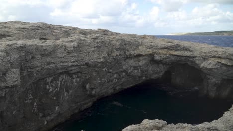 Vista-Panorámica-De-La-Cueva-De-La-Laguna-De-Coral-En-Malta-Llena-De-Agua-Profunda-En-Un-Día-Ventoso