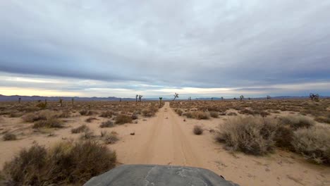A-sun-damaged-hood-of-a-vehicle-as-it-drives-down-a-dirt-road-in-the-Mojave-Desert-into-the-sunset