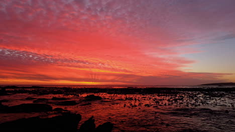 Orange-illuminated-clouds-and-ocean-reflection,-vibrant-coastal-sunset