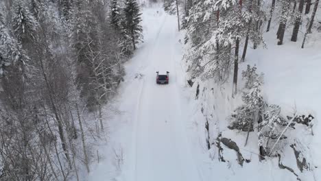 Aerial-View-Of-Car-Driving-In-The-Snowy-Road-Through-The-Forest-At-Winter