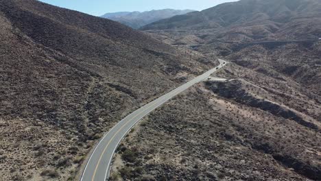 Desert-mountain-landscape-with-winding-road-and-vehicles-driving,-aerial-shot