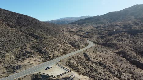 Desert-road-on-hot-sunny-day-while-vehicle-drives-by,-aerial-drone-shot