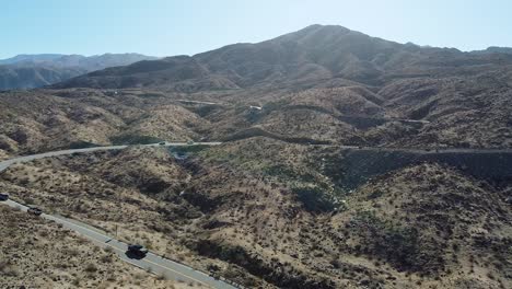 Vehículos-Que-Circulan-Por-La-Carretera-Del-Desierto-En-Un-Día-Caluroso-Y-Soleado-En-California,-Toma-Aérea-De-Drones