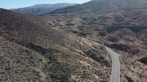 Desert-mountain-landscape-and-winding-highway,-aerial-ascend-shot
