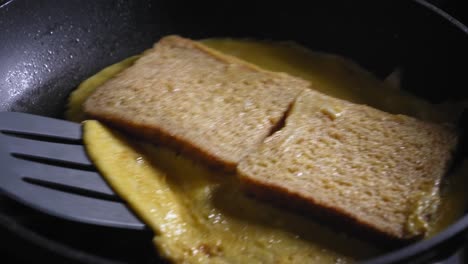 A-close-up-shot-of-a-cooked-omelette-and-toast-being-turned-over-in-a-frying-pan,-Bacon-and-a-slice-of-cheese-are-added-before-being-carefully-folded-into-a-perfect-gourmet-sandwich-using-a-spatula