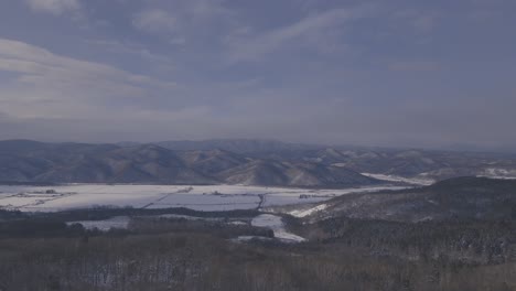 Aerial-View-Of-Winter-Farmland-Landscape-With-Mountain-Ranges-In-The-Distance-In-Hokkaido