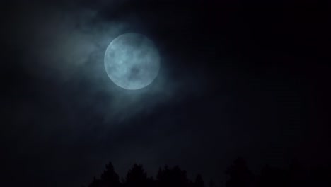Amazing-full-moon-rising-above-treetop-silhouette-with-dark-moody-clouds-passing-in-front