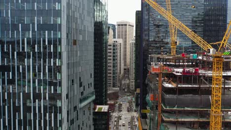 Aerial-view-between-skyscrapers-in-Seattle-with-cranes-working-on-a-construction-site