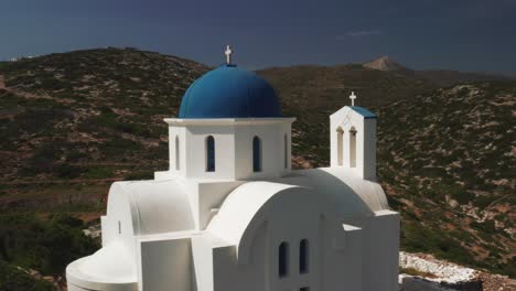 Drone-shot-of-beautiful-little-church-with-blue-dome-in-Greece-on-a-rocky-peak,-Amorgos-Island-in-cyclades-with-beautiful-panorama-of-blue-ocean-and-mountains