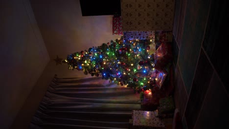 Un-árbol-De-Navidad-De-Tamaño-Mediano-Envuelto-En-Luces-De-Arcoíris-Y-Muchas-Decoraciones-Se-Sienta-Con-Muchos-Regalos-A-Su-Pie