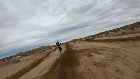 Folgen-Sie-Einem-Offroad-Motocross-Bike,-Das-Auf-Einer-Rennstrecke-Vor-Dem-Hintergrund-Der-Mojave-Wüste-Springt---Luftdrohne-Aus-Der-Ego-Perspektive-In-Zeitlupe