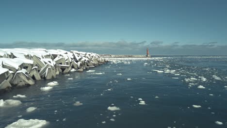 Aerial-Over-Floating-Ice-Drift-Beside-Breakwall-In-Omu-Hokkaido-With-Red-Lighthouse-In-Background