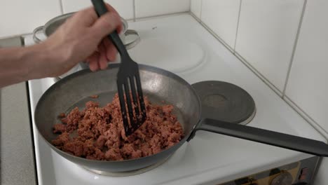 Man-frying-minced-meat-in-a-frying-pan-on-an-electric-stove