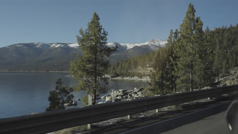 Driving-through-beautiful-Lake-Tahoe-landscape-with-view-of-mountains-and-lake-from-car-as-guardrail-and-oncoming-car-passes-by