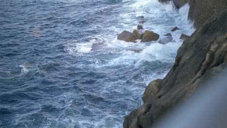 Waves-crashing-against-the-rocks-on-a-European-shoreline-of-a-during-sunset-in-San-Sebastian-Spain,-handheld-shot