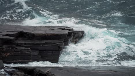 Heavy-waves-hit-the-dark-jagged-rocks-on-the-shoreline