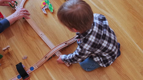 Mother-helps-child-to-build-a-toy-train-track
