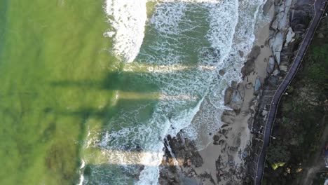 We-fly-over-a-gorgeous-lime-green-ocean-with-hints-of-blue-that-meets-with-pale-white-sand-cut-up-from-dark-shadows-being-cast-from-the-apartments-buildings-blocking-the-setting-afternoon-sun