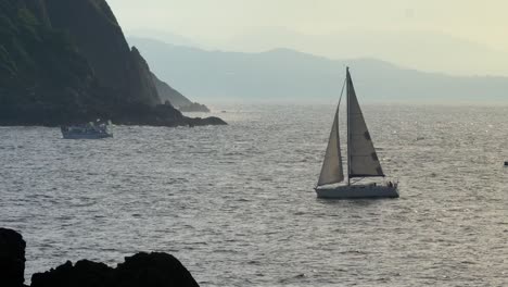Sailboat-returning-to-the-harbor-on-a-sunny-afternoon-with-golden-light-coming-through,-San-Sebastian-Spain,-static-shot